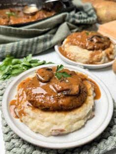 two white plates topped with mashed potatoes covered in gravy and mushroom sauce