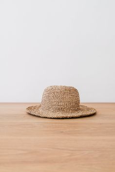 Front view of Handwoven Hat on an Oak Dining Table Against a White Wall. - Saffron and Poe Summer Packable Bucket Hat, Summer Packable Brimmed Bucket Hat, Adjustable Packable Summer Bucket Hat, Packable Summer Bucket Hat, Summer Bucket Hat With Curved Brim, Packable, Summer Bucket Hat With Curved Brim And Packable, Summer Bucket Hat With Packable Curved Brim, Summer Bucket Panama Hat For Travel, Packable Short Brim Bucket Hat For Vacation