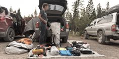 a man standing in the back of a truck next to a pile of camping gear