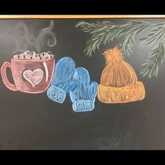 a chalk board with two knitted mittens and a cup of hot chocolate