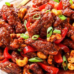 a white plate topped with meat covered in sauce and green onions next to a wooden spoon