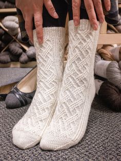 a person wearing white socks and holding their hands on the bottom of one leg while standing in front of a pile of yarn