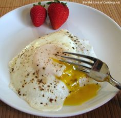 two strawberries sit on a table next to a plate with eggs