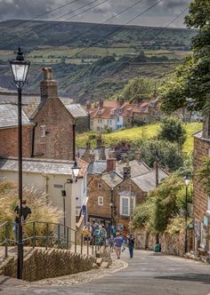 people are walking up and down the street in this small town with hills behind them