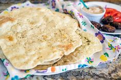 two pita breads sitting on top of a paper wrapper next to some vegetables