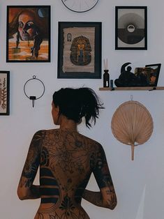 a woman with tattoos standing in front of a wall full of pictures and art on it