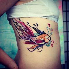 a woman's stomach with a colorful fish tattoo on her side ribcage