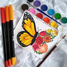 some paint and markers are laying next to a butterfly on a sheet of white paper