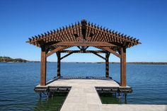 a wooden gazebo sitting on top of a lake next to a pier under a blue sky