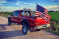 a red truck with an american flag on it's bed in the middle of a dirt road