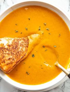 a white bowl filled with soup and grilled cheese on the top, next to a spoon