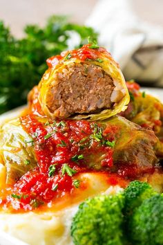 stuffed cabbage rolls on top of mashed potatoes with sauce and broccoli in the background