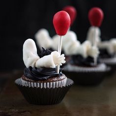 cupcakes with white icing and red candy decorations on top are sitting on a table