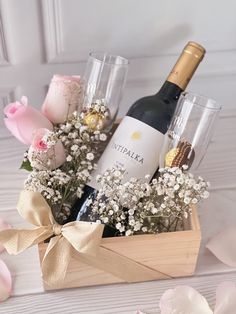 a bottle of wine and two glasses in a wooden box with flowers on the table