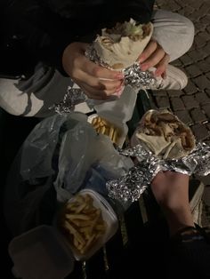 a person sitting on a bench holding food in their hands and wrapped in tin foil