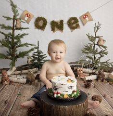 a baby sitting in front of a cake on top of a wooden table next to christmas trees