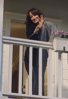 a woman standing on the balcony talking on her cell phone and waving to someone behind her