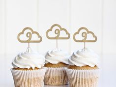 three cupcakes with white frosting and wooden toppers in the shape of clouds