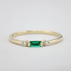 "Handmade by an inspired jewelry artist team with decades of experience in the craft of jewelry making. Each gemstone, each diamond is carefully picked. Using only the finest raw materials and the highest industry standard in manufacturing, design and finish. Sleek and sophisticated baguette Emerald and diamond ring. This rings dainty nature adds to its charm, the Emerald is elegantly set surrounded by two round diamonds adding to its slim design and elongating the ring. This dainty ring is perf Modern Diamond Ring With Birthstone, Dainty Emerald Cut Ring With Diamond Accents, Emerald Rings With Single Cut Diamonds For Anniversary, Emerald Rings With Single Cut Diamonds For Gifts, Dainty Emerald Diamond Ring, Minimalist Diamond Ring With Prong Setting For May Birthstone, Minimalist Emerald Diamond Ring For May Birthstone, Dainty Emerald Ring With Diamond, Emerald Promise Ring With Single Cut Diamonds