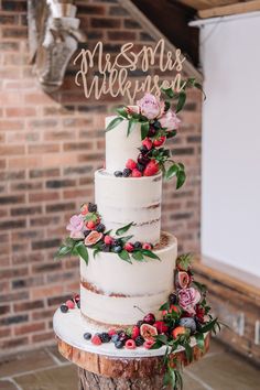 a three tiered cake with flowers and leaves sits on top of a tree stump