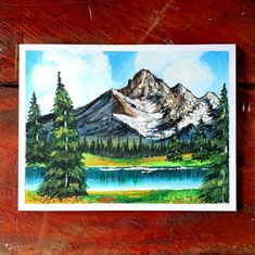 a painting of mountains and trees on a wooden surface