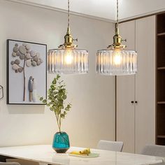 two pendant lights hanging over a dining room table with chairs and a vase on it