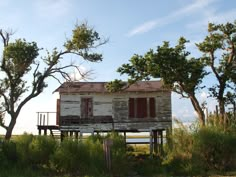 an old run down house sitting on top of a lush green field next to trees