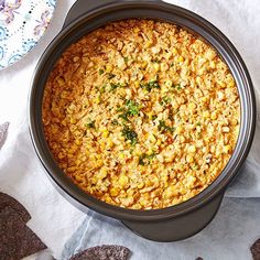 a crock pot filled with corn on top of a table next to crackers