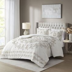 a bed with white comforter and pillows in a room next to a lamp on a table