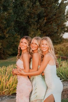 three beautiful young women standing next to each other in front of some bushes and trees