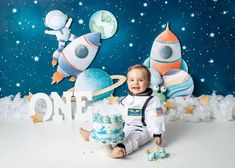 a baby boy sitting in front of a cake with space themed decorations on the wall