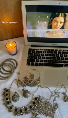 an open laptop computer sitting on top of a table next to jewelry and a candle