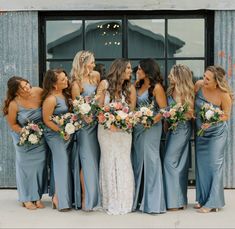 a group of women standing next to each other in front of a building holding bouquets