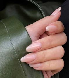 a woman's hand with pink nails holding onto a green leather bag and wearing a black jacket