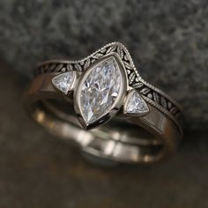 a close up of a wedding ring with a pear shaped diamond in the center and two smaller pear shaped diamonds on each side