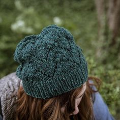 a woman with red hair wearing a green knitted hat and looking down at the ground