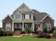 a house with red shutters and white trim on the front door is surrounded by green grass