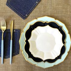 a table setting with blue napkins, silverware and gold utensils