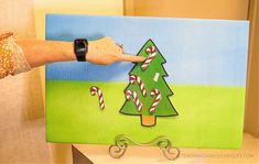 a hand is pointing at a christmas tree on a canvas that has candy canes in it