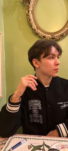 a young man sitting at a table with food in front of him and looking off into the distance