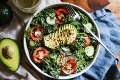 a salad with avocado, tomatoes and spinach in it on a table