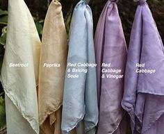 four different colors of scarves hanging from a line in front of some trees and bushes