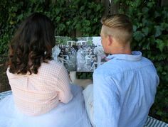 a man and woman sitting on a bench reading a magazine