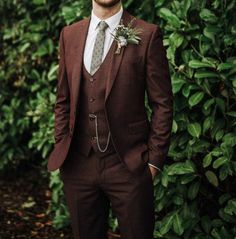 a man wearing a suit and tie standing in front of some bushes smiling at the camera