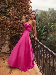 a woman in a long pink dress leaning on a railing with her hand on her hip