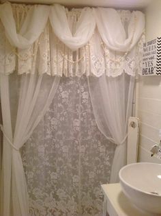 a white sink sitting under a bathroom window next to a toilet and bathtub covered in lace