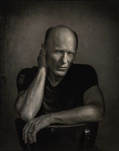 an older man sitting in a chair with his hands on his head and looking off to the side