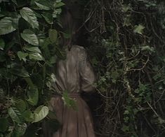 a woman standing in front of a bush with vines on it's sides and her back to the camera