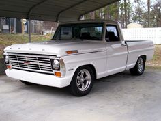 an older pickup truck parked in a carport with no roof on the ground and trees behind it