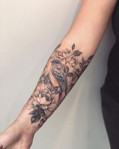 a woman's arm with a bird and flowers tattoo on her left arm,